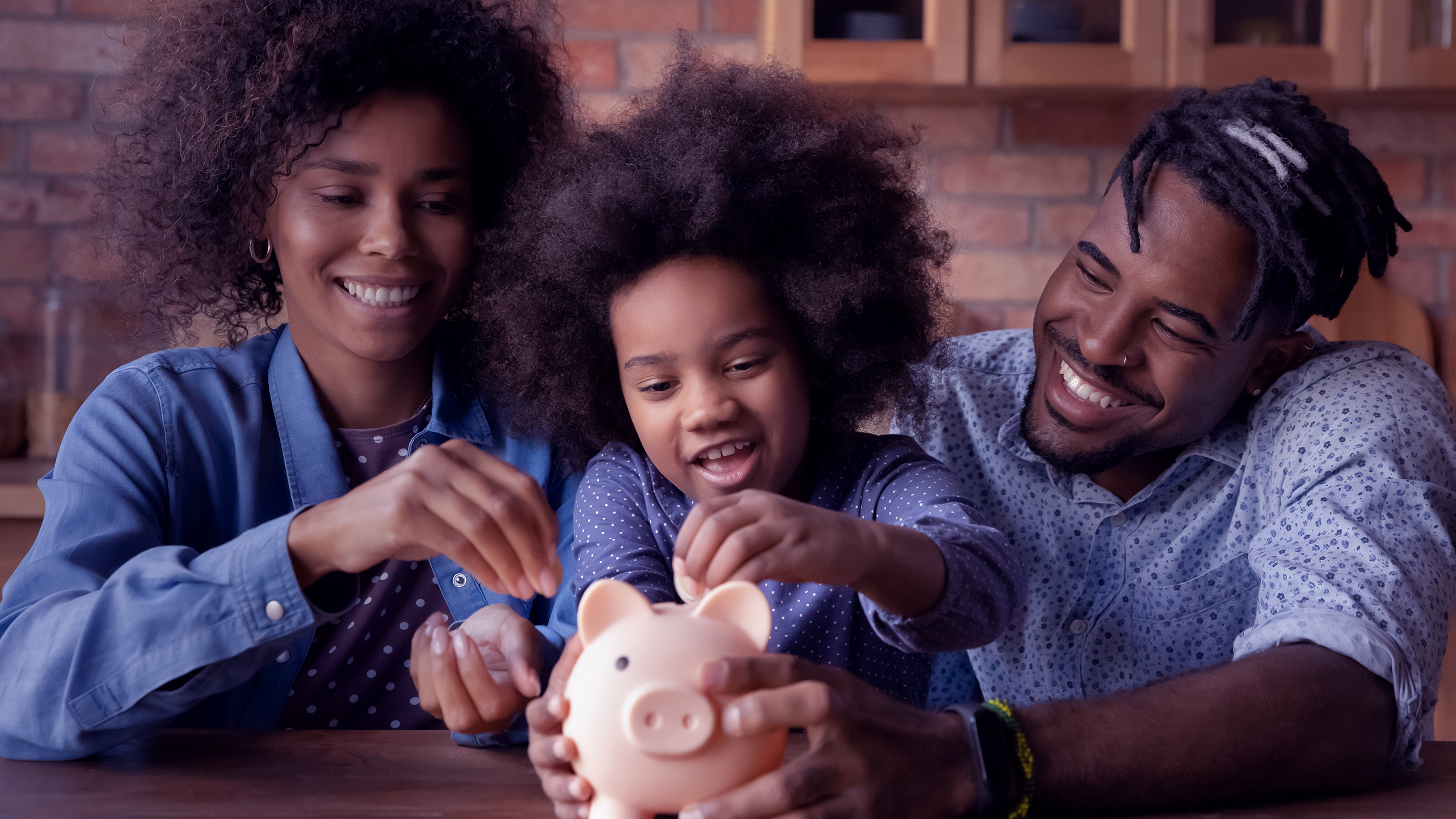 família sorrindo com uma crinaça ao centro colocando uma moeda em um cofrinho de porquinho.