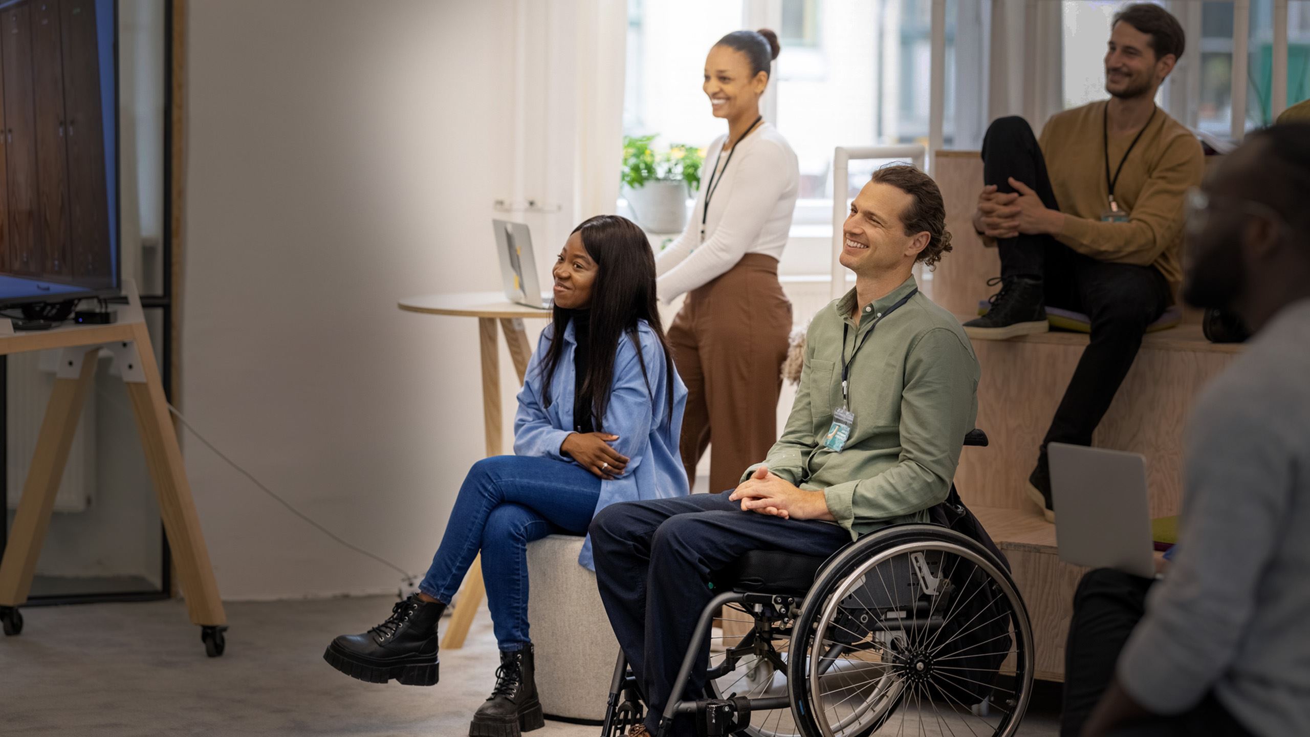 pessoas olhando para uma apresentação em um ambiente de trabalho. elas estão felizes. entre estas pessoas está um homem com mobilidade reduzida em uma cadeira de rodas
